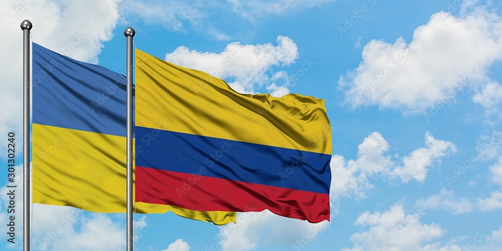 Wall mural ukraine and colombia flag waving in the wind against white cloudy blue sky together. diplomacy conce