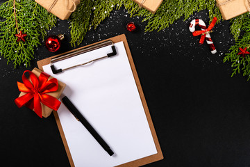 Christmas composition. Girlanda with Christmas ornaments and gifts on black background and blank notepad. Christmas, winter, new year concept. Flat lay, top view, copy space. © Julio Ricco