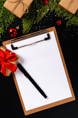 Christmas composition. Girlanda with Christmas ornaments and gifts on black background and blank notepad. Christmas, winter, new year concept. Flat lay, top view, copy space. © Julio Ricco