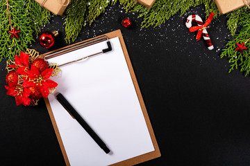 Christmas composition. Girlanda with Christmas ornaments and gifts on black background and blank notepad. Christmas, winter, new year concept. Flat lay, top view, copy space. © Julio Ricco