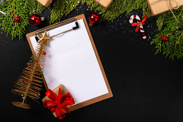 Christmas composition. Girlanda with Christmas ornaments and gifts on black background and blank notepad. Christmas, winter, new year concept. Flat lay, top view, copy space. © Julio Ricco