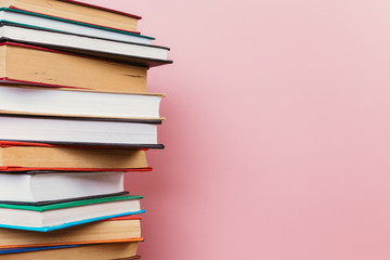 A simple composition of many hardback books, raw books on a wooden table and a pale pink background