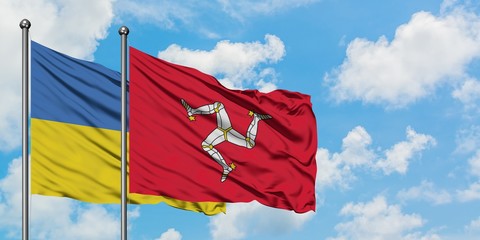 Ukraine and Isle Of Man flag waving in the wind against white cloudy blue sky together. Diplomacy...