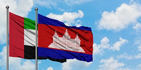 United Arab Emirates and Cambodia flag waving in the wind against white cloudy blue sky together....