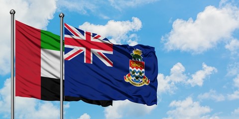 United Arab Emirates and Cayman Islands flag waving in the wind against white cloudy blue sky together. Diplomacy concept, international relations.