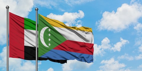 United Arab Emirates and Comoros flag waving in the wind against white cloudy blue sky together....