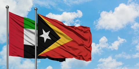 United Arab Emirates and East Timor flag waving in the wind against white cloudy blue sky together....