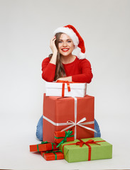  woman wearing christmas santa hat sitting on floor with pile of gift boxes.