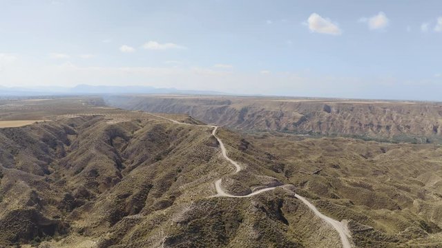 Aerial Drone wide view of dry valley and mountains at Gorafe, Desierto de los Coloraos in Blue sky, Sierra Nevada, Granada, Spain. Spanish desert canyon with vegetation, Andalusia. Lonely road, car.