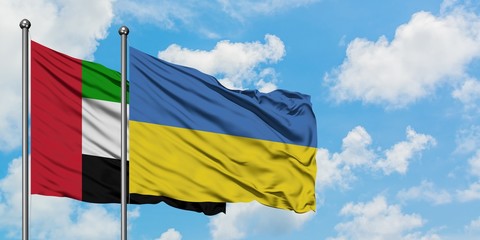 United Arab Emirates and Ukraine flag waving in the wind against white cloudy blue sky together. Diplomacy concept, international relations.