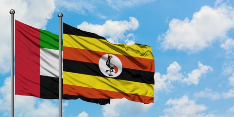 United Arab Emirates and Uganda flag waving in the wind against white cloudy blue sky together....