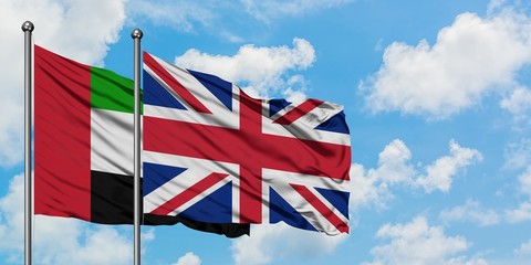United Arab Emirates and United Kingdom flag waving in the wind against white cloudy blue sky...