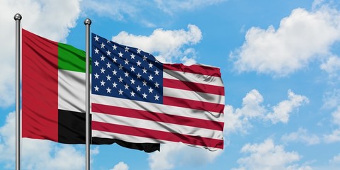 United Arab Emirates and United States flag waving in the wind against white cloudy blue sky...