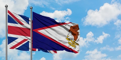 United Kingdom and American Samoa flag waving in the wind against white cloudy blue sky together....