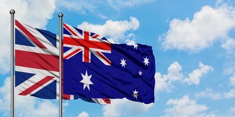 United Kingdom and Australia flag waving in the wind against white cloudy blue sky together....