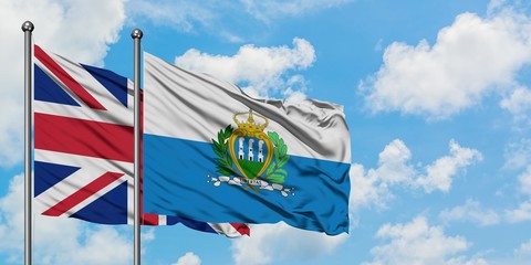 United Kingdom and San Marino flag waving in the wind against white cloudy blue sky together....