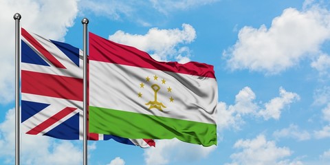 United Kingdom and Tajikistan flag waving in the wind against white cloudy blue sky together....