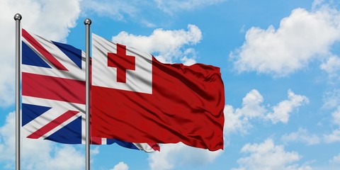 United Kingdom and Tonga flag waving in the wind against white cloudy blue sky together. Diplomacy...