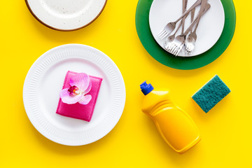Dishwashing liquid bottle near plates on yellow background top view