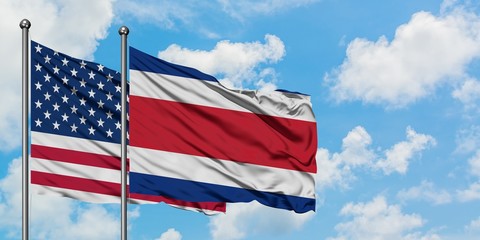United States and Costa Rica flag waving in the wind against white cloudy blue sky together....