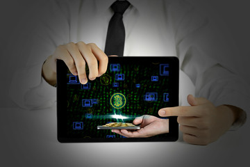 Businessman holding a tablet with bitcoin symbol and laptop icons on binary background