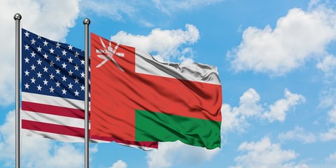 United States and Oman flag waving in the wind against white cloudy blue sky together. Diplomacy concept, international relations.