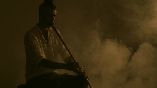 38 years old middle Eastern  Reed Flute or Ney Instrument player Playing a Reed Flute in smoke.