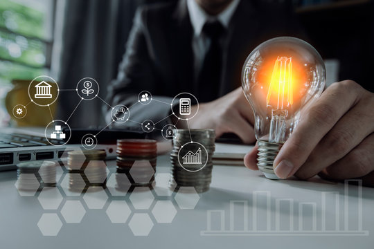 Double exposure of graph and rows of coins for finance and business concept. business man hand holding lightbulb with using calculator to calculate and money stack. Out of focus.  - Powered by Adobe