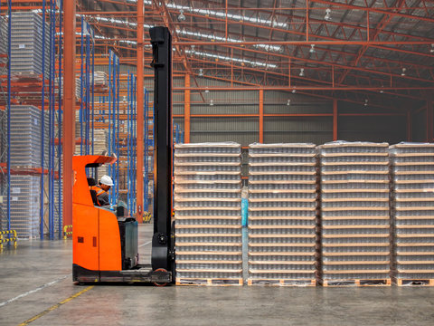 The warehouse worker using reach fork truck lifting pallet with bottle from tall rack to prepare area before pick up to delivery.