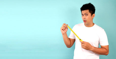Asia Man holds a tape measure on the blue background in studio  with copy space.
