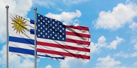 Uruguay and United States flag waving in the wind against white cloudy blue sky together. Diplomacy concept, international relations.