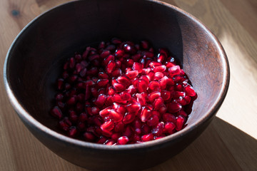 Pomegranate Seeds in Wooden Bowl with  Natural Sunlight and Pastel Yellow Tablecloth. Natural Sunlight.