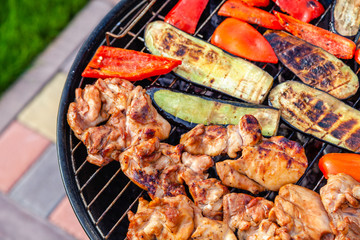 Assortment of fresh healthy colored vegetables, chicken meat grilled on BBQ grilling over a hot fire coals against green grass on barbecue. Concept summer party, outdoor meal, open air cook