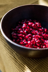 Pomegranate Seeds in Wooden Bowl with  Natural Sunlight and Pastel Yellow Tablecloth. Natural Sunlight.