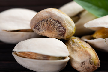  Pistachio in wooden bowl in background with green leaves.