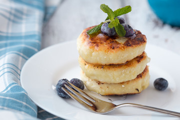Cottage cheese pancakes on a dark background. Syrniki with fresh mint. Pancakes with cottage cheese on a lilac plate . Homemade food.