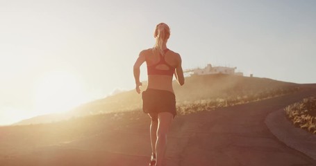 Fit attractive woman running at sunset with golden cloud haze atmosphere, amazing sunset workout in the mountains, determined runner training at sunset