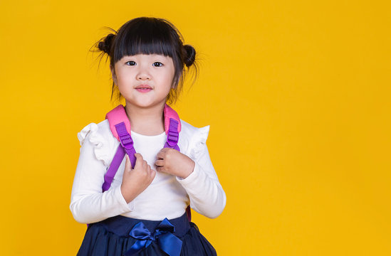Portrait of young happy little asian girl in uniform isolated on yellow background with copy space. Education for toddler or preschool, childhood lifestyle back to school concept
