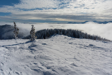 Beautiful scenery with winter snow-capped mountains, with fogs and contrasting snow structure and red tourist tent in the foreground, in locations in the Ukrainian Carpathians.