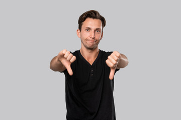 Upset handsome young man in a black t-shirt holding thumbs down showing his evaluation.