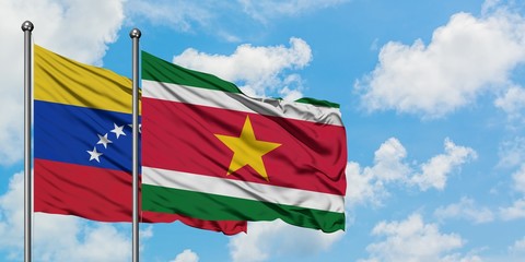 Venezuela and Suriname flag waving in the wind against white cloudy blue sky together. Diplomacy concept, international relations.