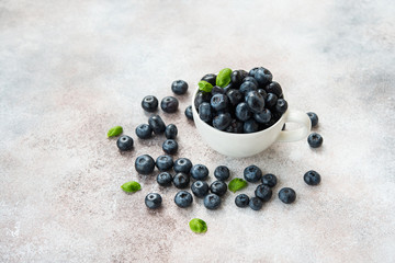 Blueberries lie in a Cup and scattered on a concrete table. Summer seasonal product. Healthy vegetarian dessert.