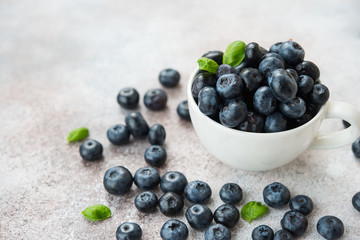 Blueberries lie in a Cup and scattered on a concrete table. Summer seasonal product. Healthy vegetarian dessert.