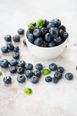 Blueberries lie in a Cup and scattered on a concrete table. Summer seasonal product. Healthy vegetarian dessert.