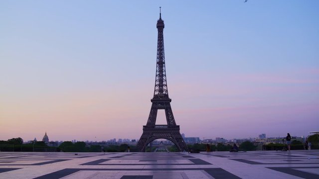 Eiffel tower at sunset orange blue sky in Paris during the summer. Haussmanian buildings, trees, 16th, symbol, trocadero, architecture, landmark, historic, birds. Tracking in 4K UHD.