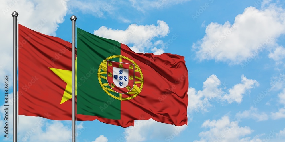 Wall mural vietnam and portugal flag waving in the wind against white cloudy blue sky together. diplomacy conce