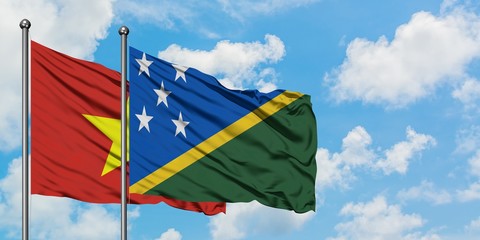 Vietnam and Solomon Islands flag waving in the wind against white cloudy blue sky together....