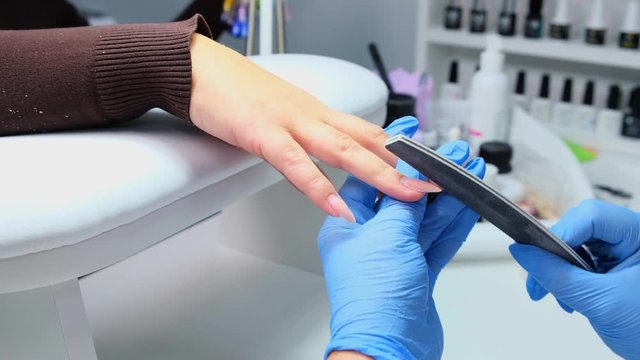 Closeup shot of a woman in a nail salon receiving a manicure by a beautician with nail file. Woman getting nail manicure. Beautician file nails to a customer.