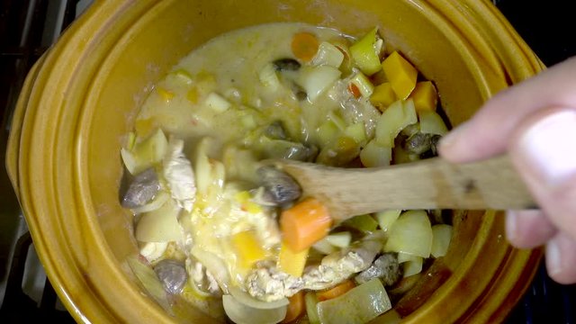 Slow Motion Close POV Overhead Shot Of A Man’s Hands Lifting A Ceramic Lid With An Oven Glove, Then Stirring The Chicken And Vegetable Casserole In The Slow Cooker With A Wooden Spatula. 