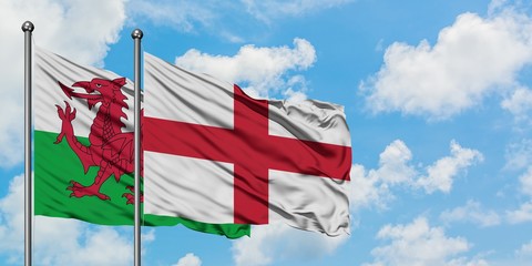 Wales and England flag waving in the wind against white cloudy blue sky together. Diplomacy...